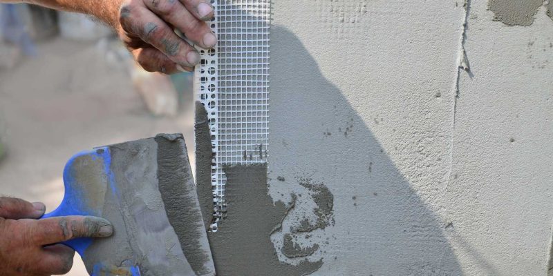 Hands of an old manual worker with wall plastering tools renovating house. Plasterer renovating outdoor walls and corners with spatula and plaster. Wall insulation. Construction finishing works